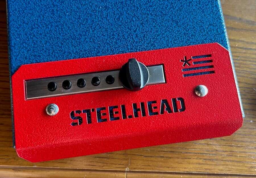 : Close-up of the Simplex-style mechanical lock on the red and blue Steelhead pistol box.