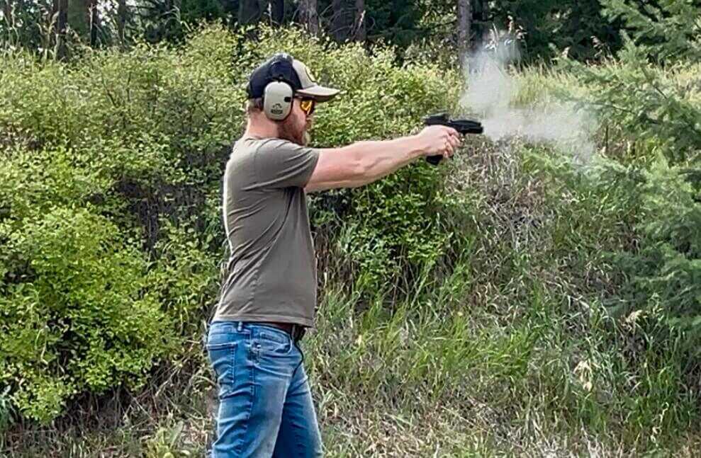 A man in jeans is shooting a ported handgun in the forest.