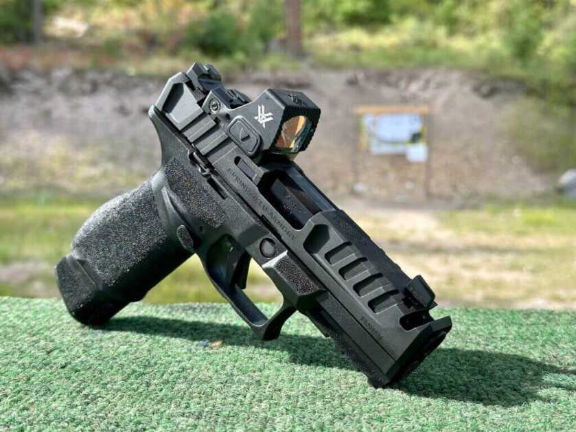 A black handgun rests on a green table at the range.  Echelon 4.0C Comp