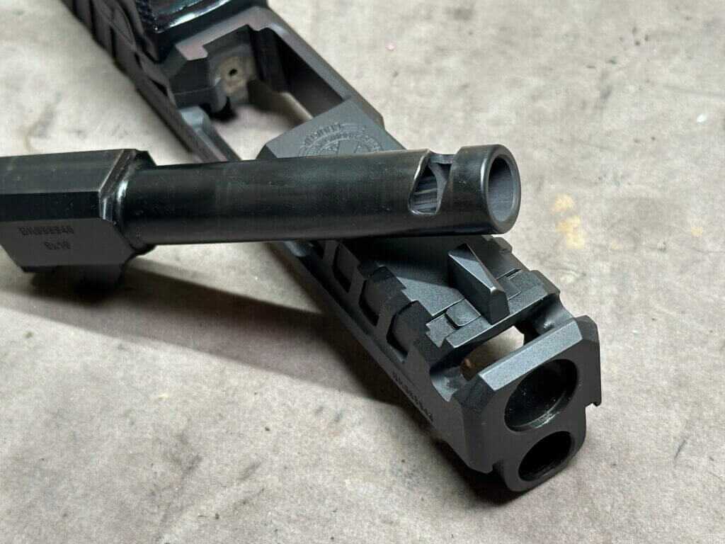 The barrel is removed from a pistol slide and we can see the port machined into the end of the barrel.