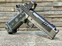 A handgun with an optic on it is posed in front of a stone wall.