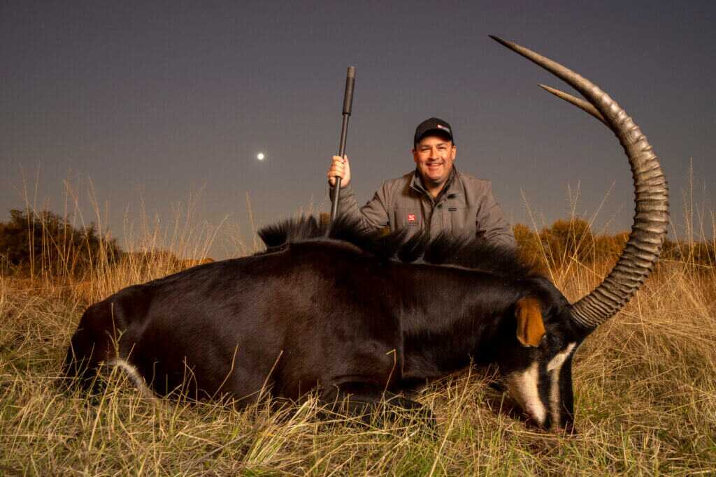 Brandon Maddox with suppressed rifle after a hunt at dusk in South Dakota grass