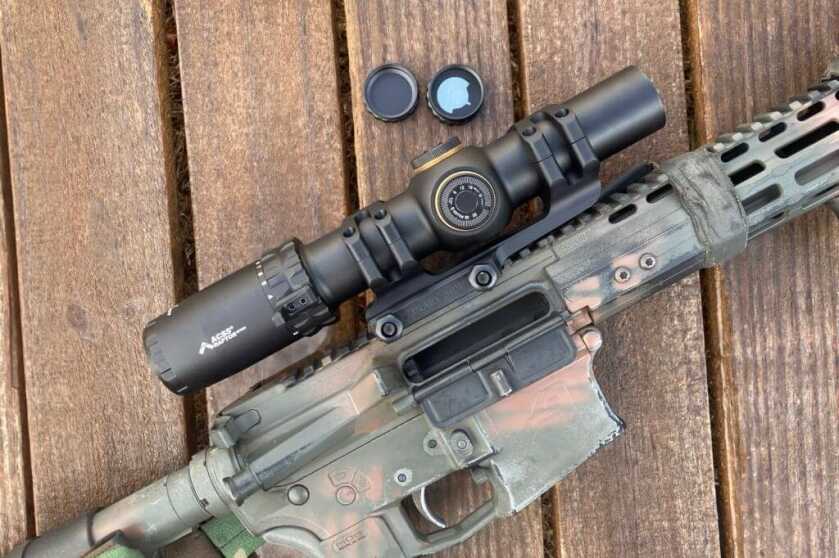 Rifle scope windage turret cap removed, showing integrated spare CR2032 battery storage in the cap.
