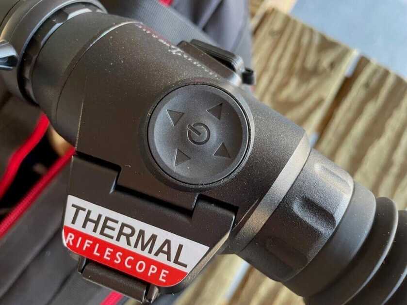 3 - Heating Seeking Optic: Sight Mark Wraith Mini Thermal large button on top of the Wraith Mini Thermal with wood n the background