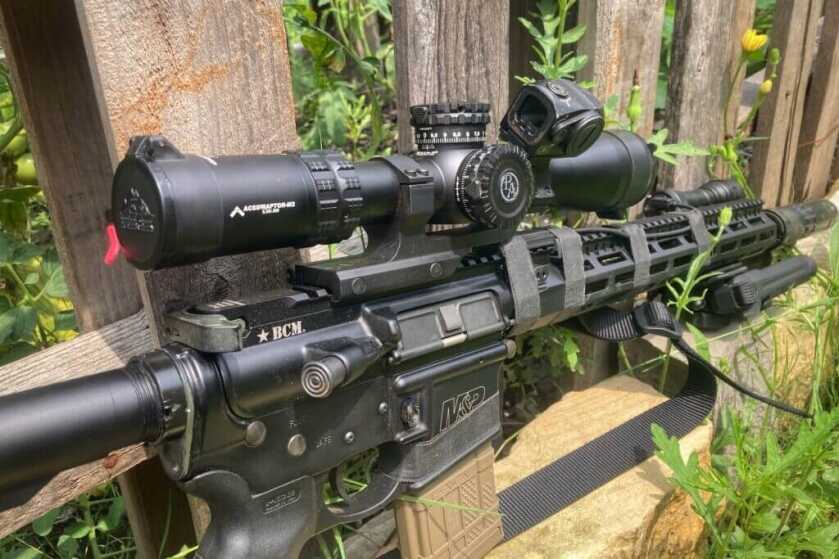 Primary Arms GLX 2.5-10 on rifle in front of wood fence and green plants