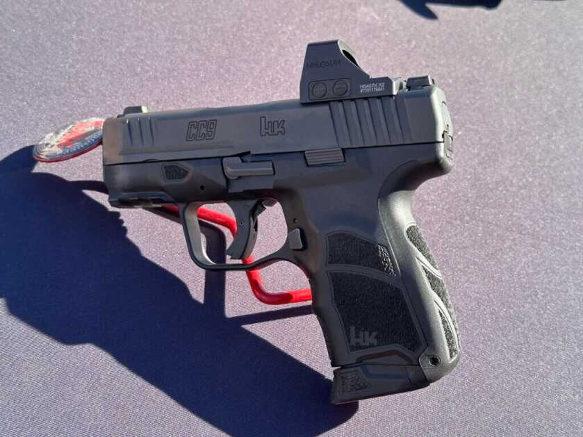 A handgun is propped up on a black table with a red stand. The handgun is pointing to the left.