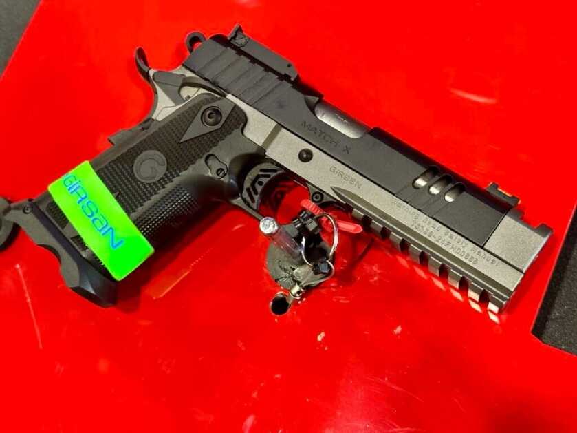 A black and grey handgun rests on a red background, pointing down and to the right.