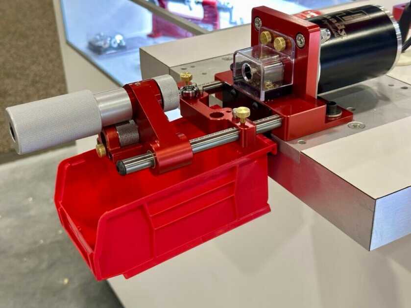A red and silver case trimmer is mounted to a table. The motor is stationary and the cartridge holder is on sliders.