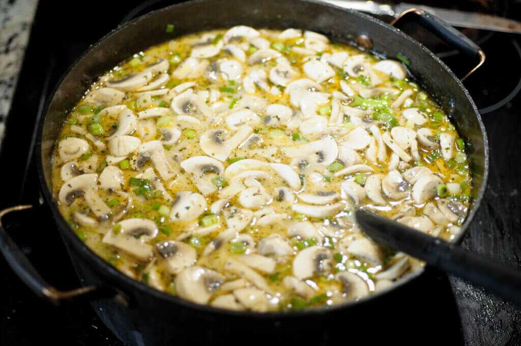 soup in a pot on the stove with mushrooms and onions on top.