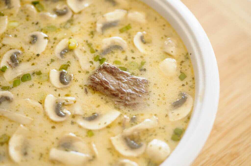 soup in a bowl with a piece of meat and mushrooms on top.