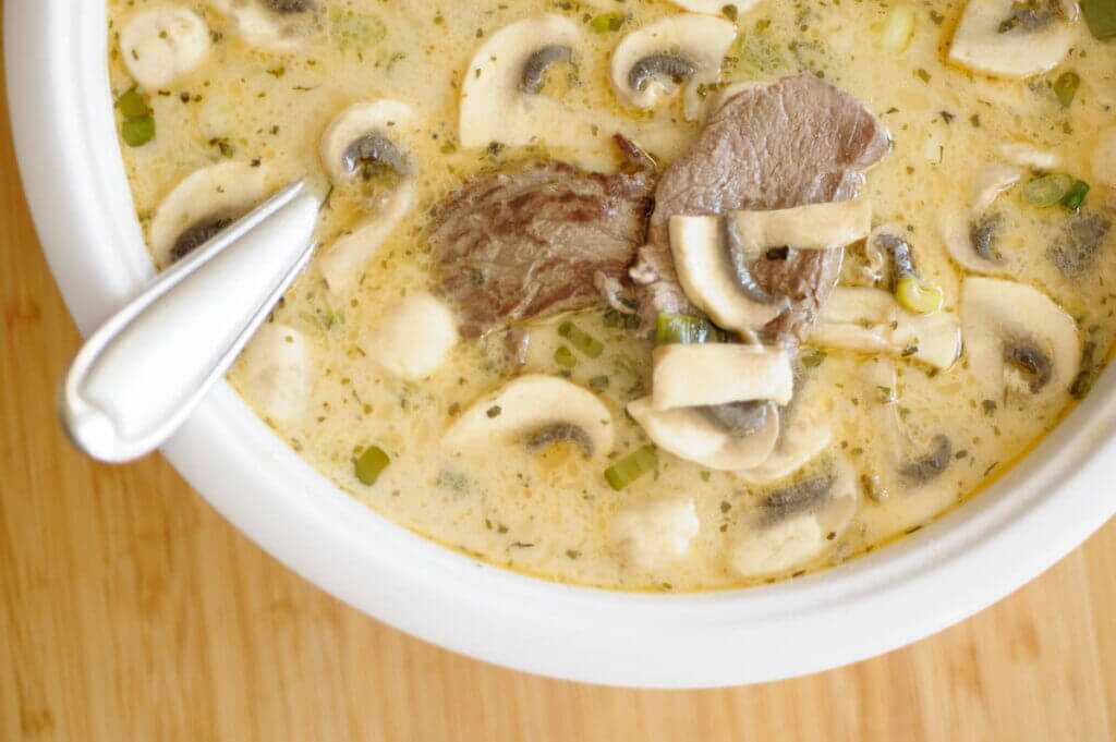 soup in a white bowl with a spoon handle sticking out sitting on a table.