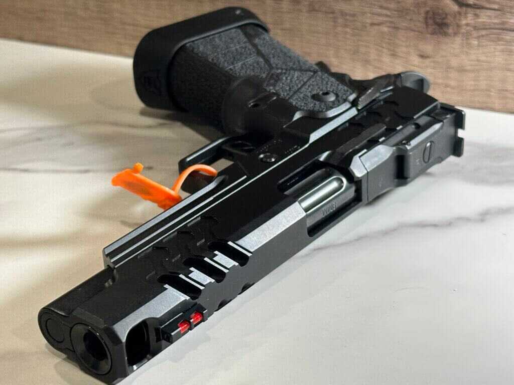 There is a black handgun with the muzzle facing toward us laying on a white granite countertop. This handgun has a big port in the slide and barrel right behind the muzzle. 
