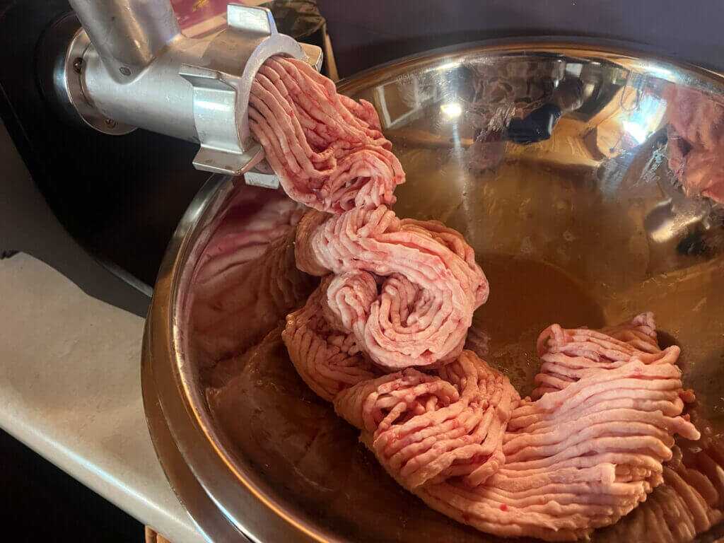 Chilled bear fat coming out of a meat grinder into a steel bowl before rendering bear grease