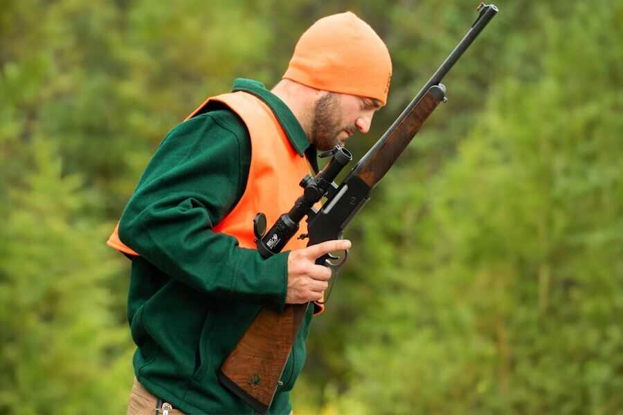 Hunter wearing blaze orange and carrying a Henry Long Ranger Big Woods Carbine while moving through dense timber during a whitetail hunt.