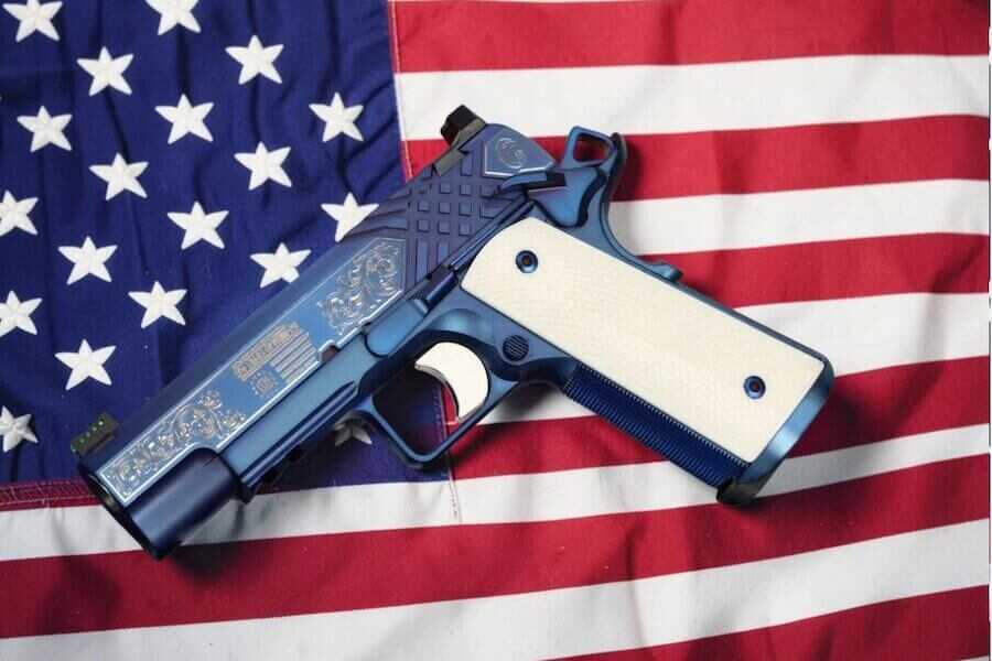 The SK Guns "250 Years of Freedom" 1911 Commander in .45 ACP is displayed atop an American flag, showcasing its sapphire PVD finish, ivory-colored grips, and patriotic engravings commemorating the United States' 250th anniversary.