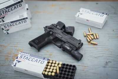 Staccato 2011 pistol with optic and weapon light surrounded by ammunition at a shooting range
