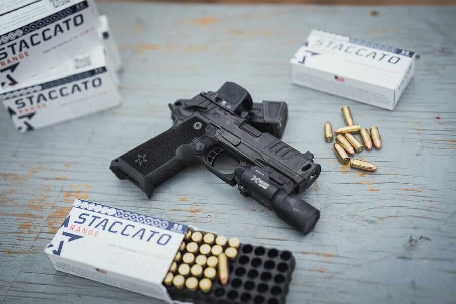 Staccato 2011 pistol with optic and weapon light surrounded by ammunition at a shooting range