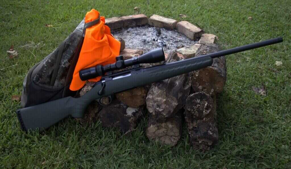 Glenfield Model A 6.5 Creedmoor hunting rifle beside an orange hunting vest and backpack
