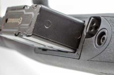The magazine release lever is inset just forward of the magazine well.