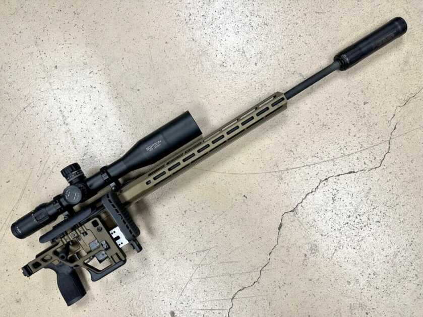 A rifle with a folding stock and suppressor lays on a concrete floor.