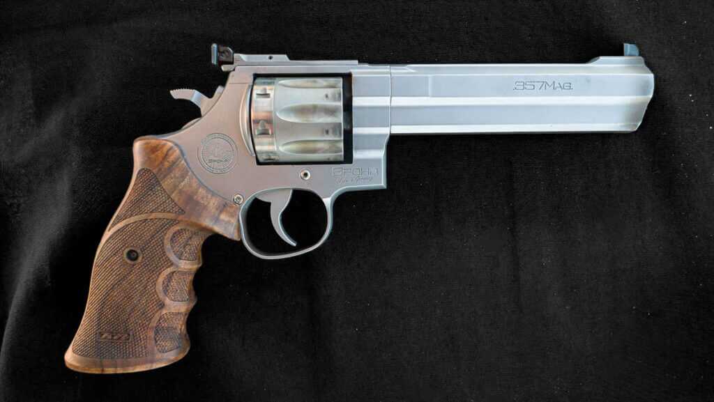 The revolver laying on a black cloth on a table. The right side is facing up with the gun pointed ot the right.