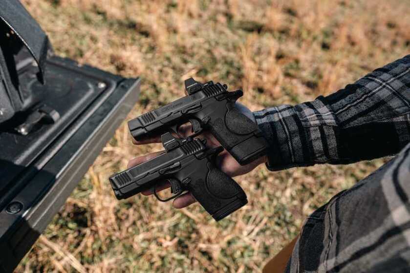 A hand holding two Smith & Wesson CSX pistols.