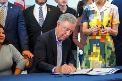 Gov. Ned Lamont signing legislation in front of a crowd.