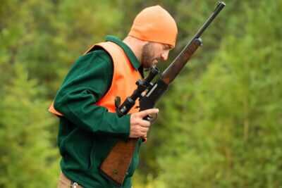 Hunter wearing blaze orange and carrying a Henry Long Ranger Big Woods Carbine while moving through dense timber during a whitetail hunt.