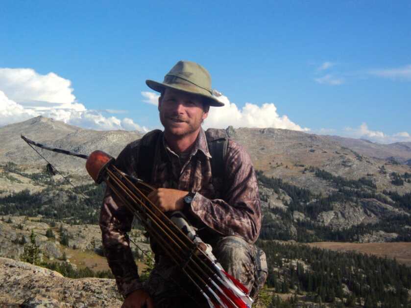 TAKE THE SHOT: A traditional bowhunter is offered a mid-range shot at a moving bull elk. Should he take the shot? Hunter with bow and quiver posing in front of mountain range