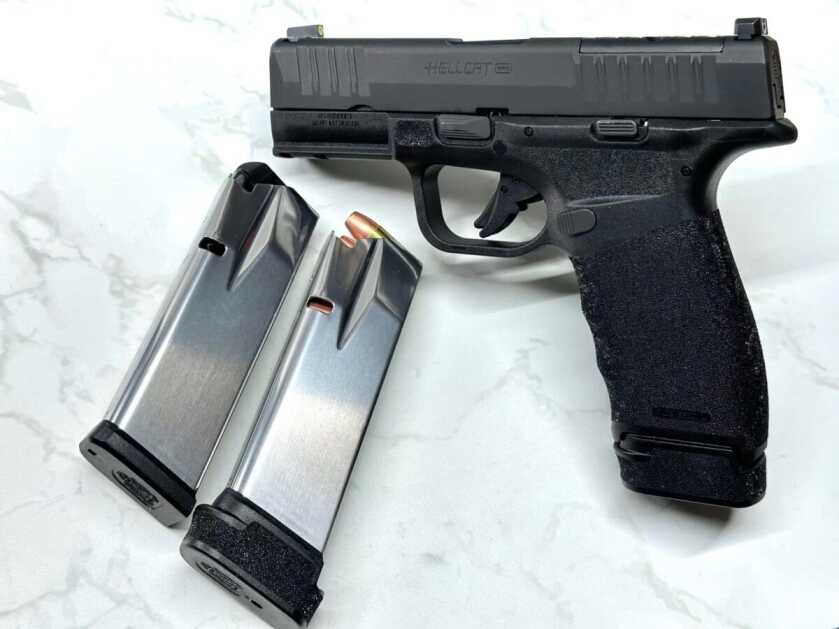 Holy Hellcat! Petite Pistol With Insane Upgraded Magazine Capacity Two silver magazines lay next to a propped up black handgun.