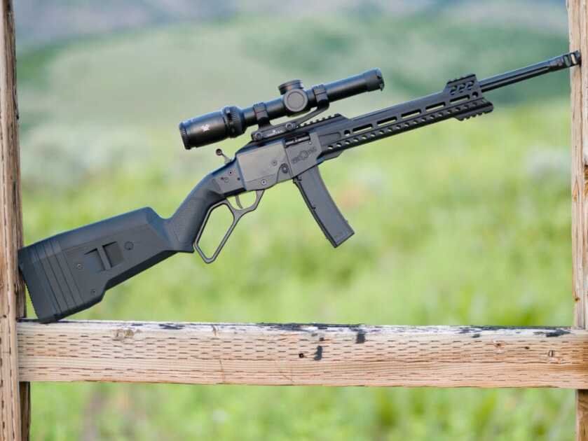 POF Tombstone 9mm shown in profile  with a Vortex LPVO and positioned between two fence posts with a grassy mountainside in the background.