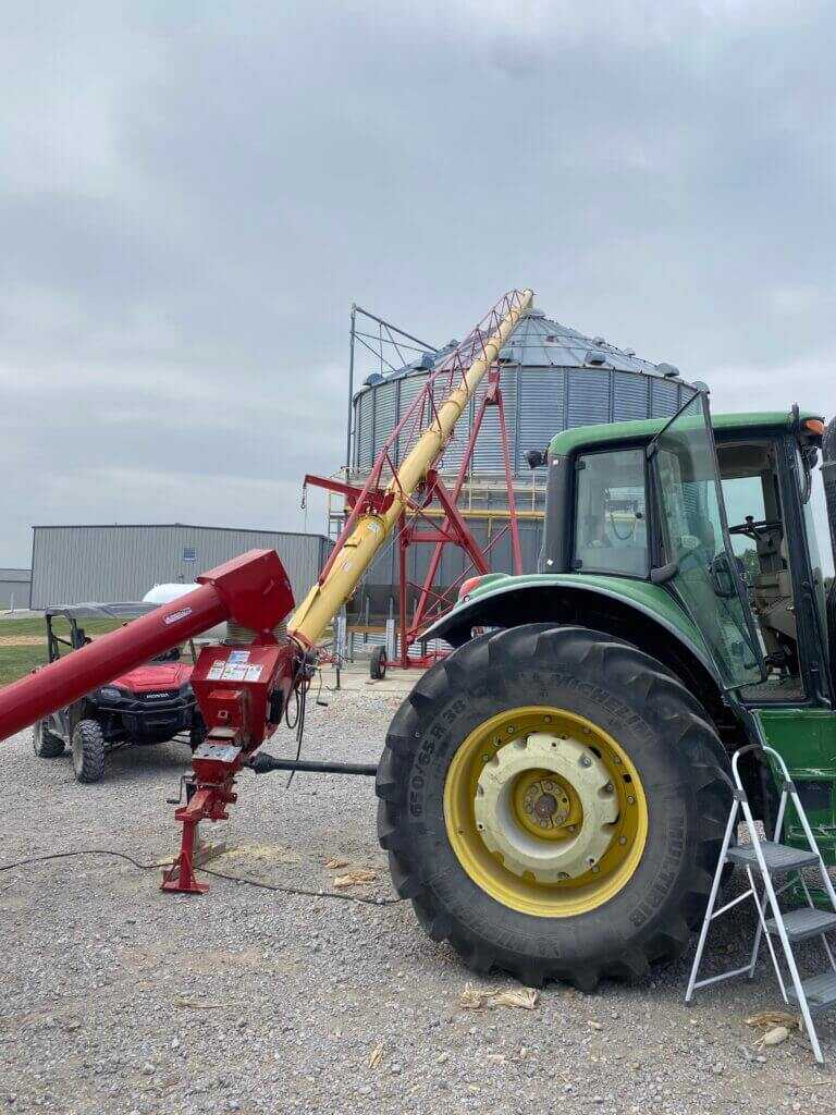 tractor powering auger beside grain bins during dusty harvest conditions on duck hunting access farm