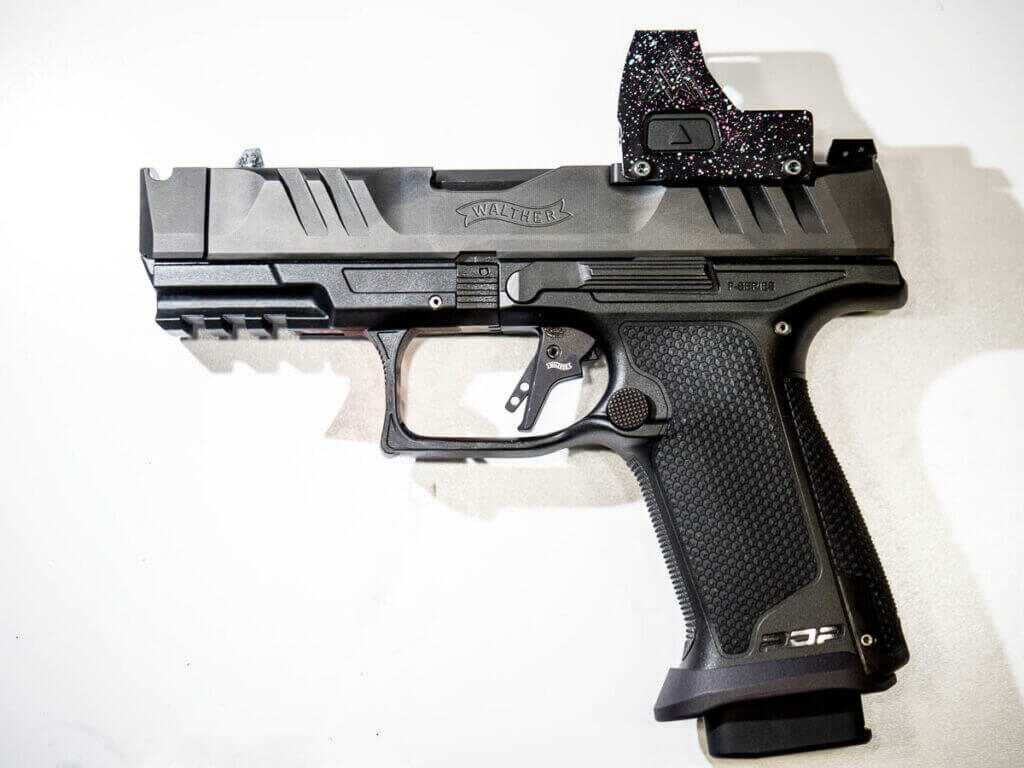 The gun is laying on a white table, facing to the left, the whole gun is visible. small hands