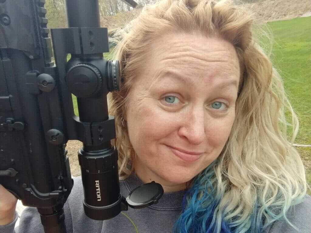 blond woman with rifle in front of grass field