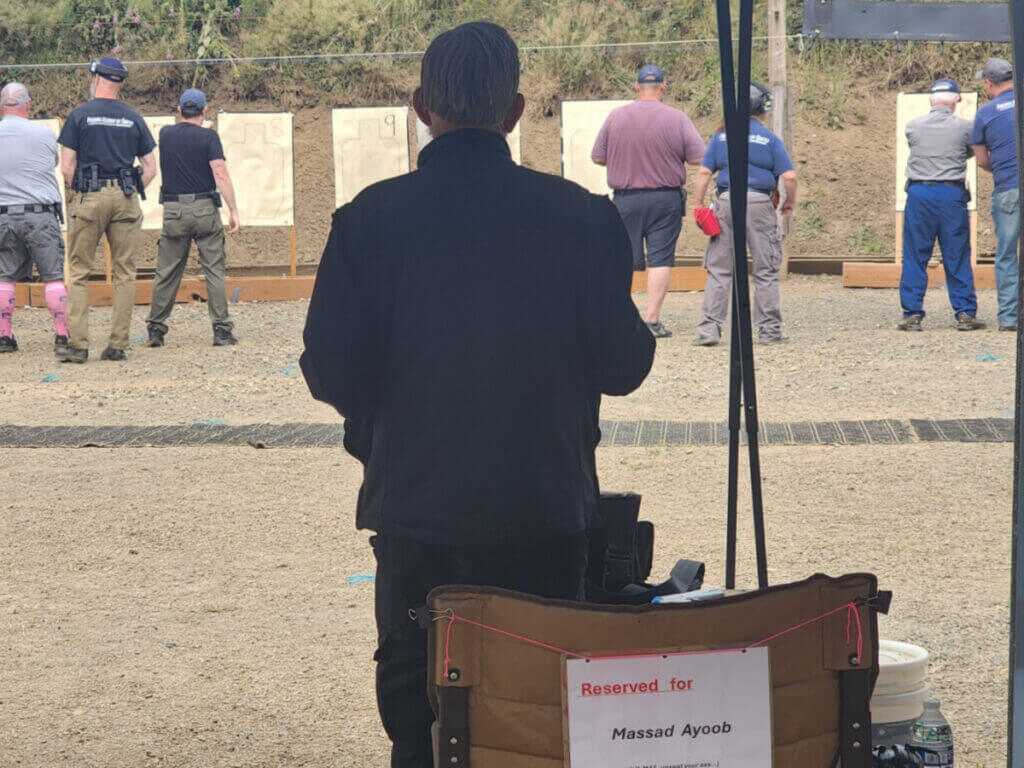 Man in jacket oustide at gun range under shelter during live fire class