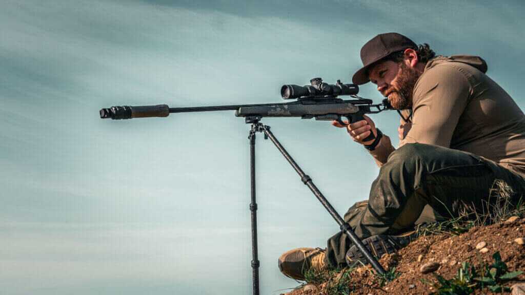 man with a rifle and a bipod sitting on a hill
