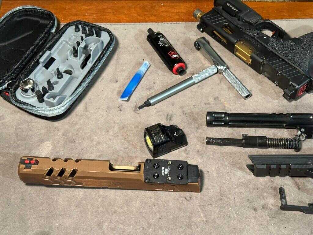 Pistol parts are scattered on a workbench where the Smart-Torq wrench and driver are being used to install or remove various parts. 