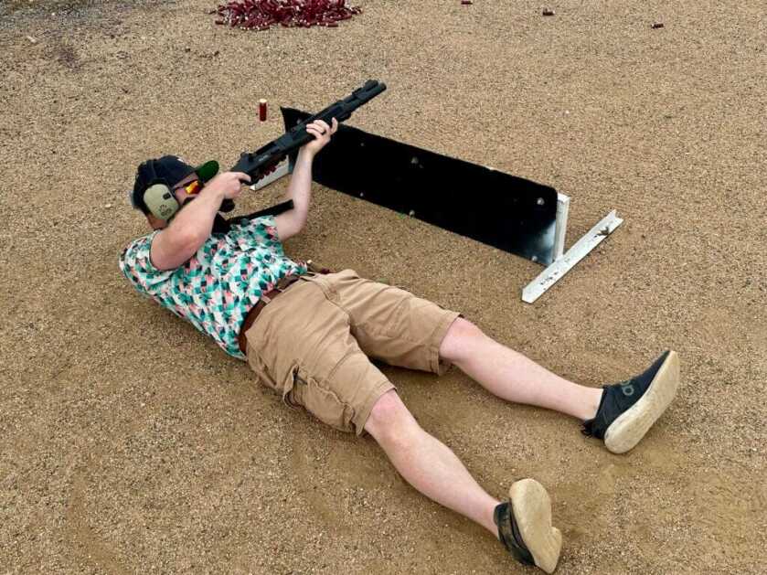 A man lays on his back, shooting a shotgun over low cover. 940 Pro Tactical SPX