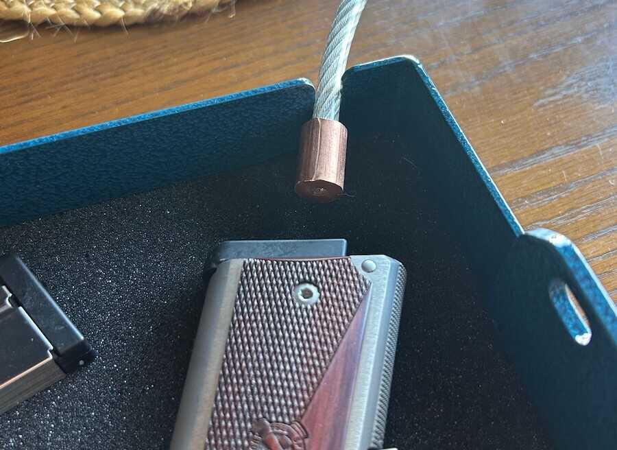 Close-up view of the security cable inserted into the lock box corner next to a handgun.