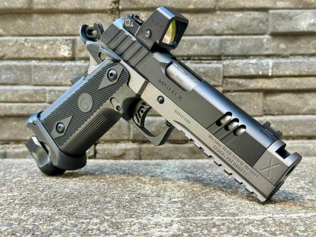 A pistol with mounted optic is posed in front of a stone background.