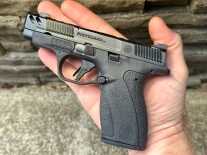 A small handgun is positioned in the palm of a man's hand.