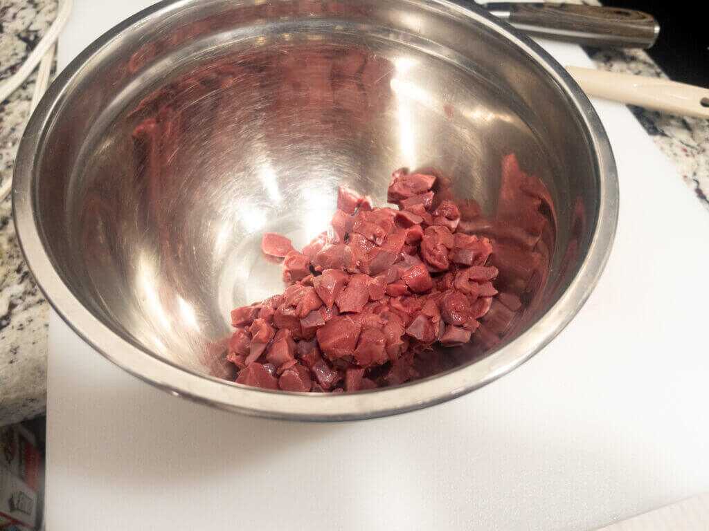 Diced elk heart coated in oil and seasoning in a steel bowl.