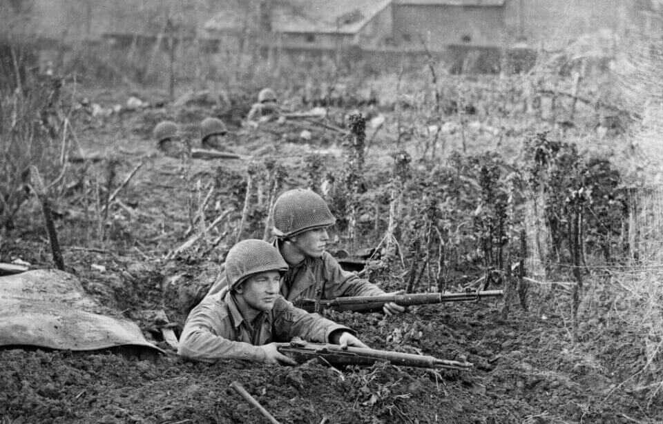 World War II GIs in foxholes with M1 Garand rifles at the ready
