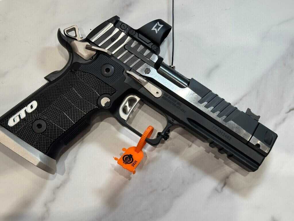 A black gun with silver accents rests on a marble counter top.
