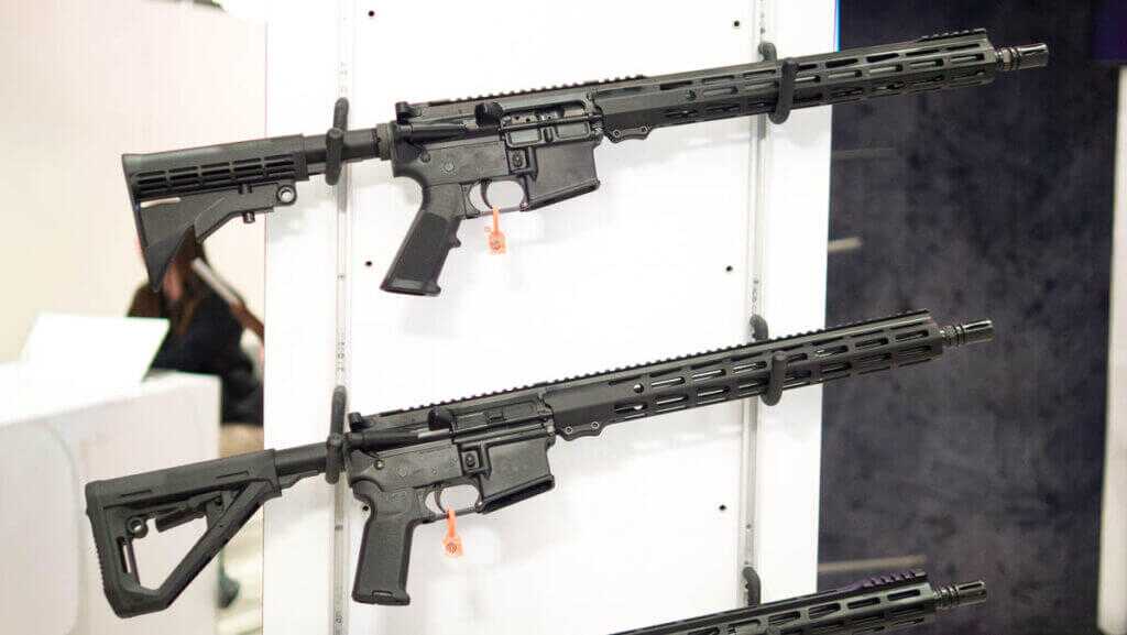 two AR-15s hanging on a white wall rack pointing right.