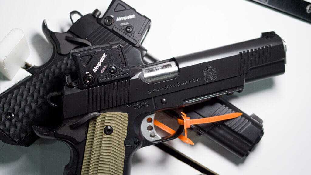 two 1911s laying on top of each other on a white table facing right with COA sights.