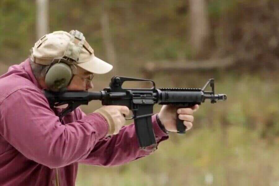 A man in a purple shirt shooting what appears to be a machine gun.