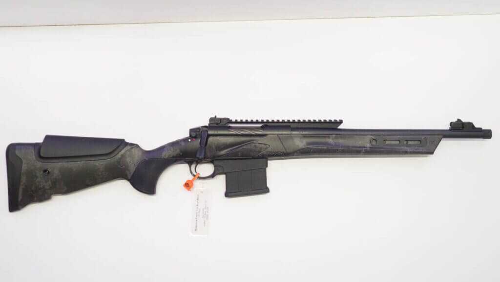 The whole rifle lying on a white table facing to the right.