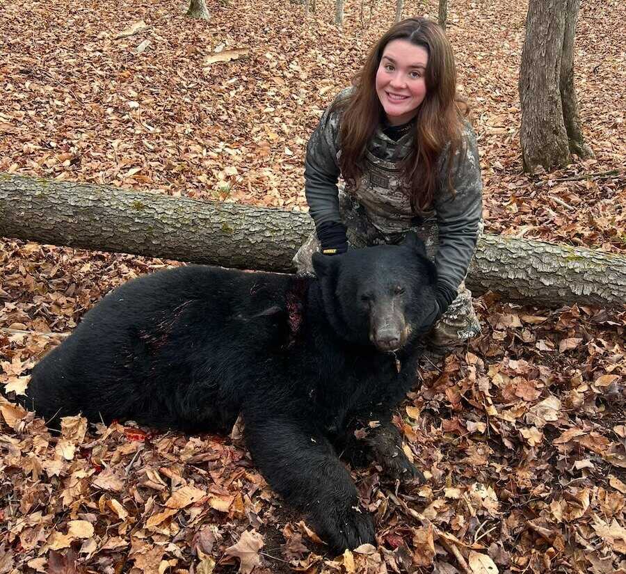 Hunter Janelle Miller kneeling beside her harvested black bear in the woods of Freedom, New York.