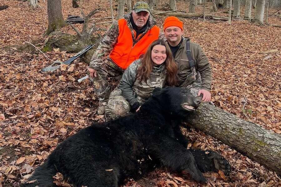 Janelle Miller with her father and grandfather posing behind her harvested black bear in Freedom, New York.
